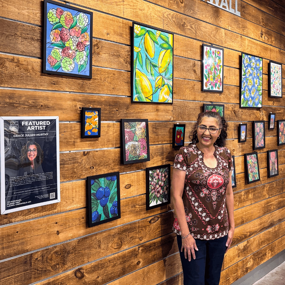 Female artist standing in front of wooden wall featuring a brightly colored collection of original artwork.